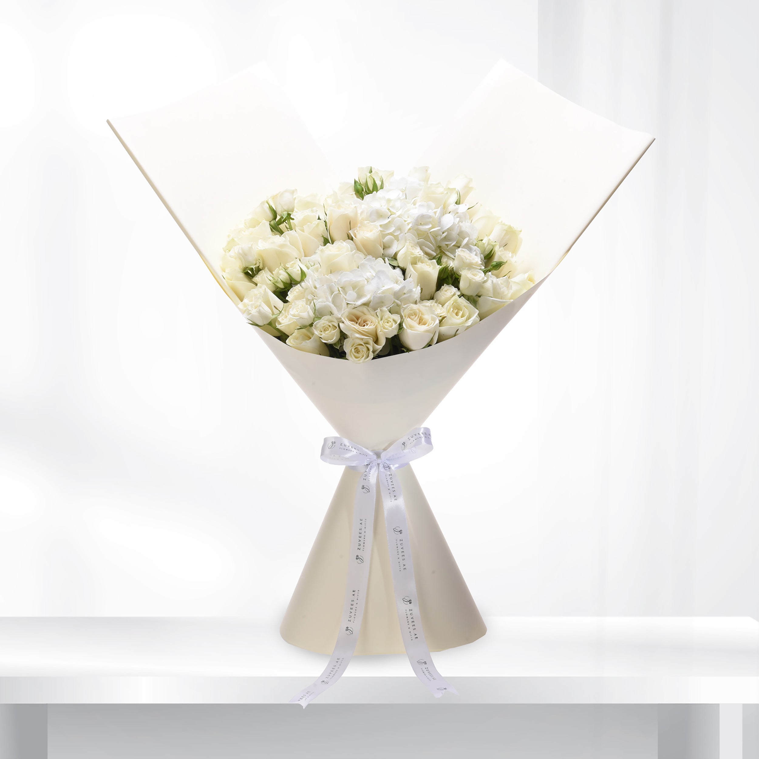 Elegant white rose and hydrangea bouquet wrapped in cream paper with branded ribbon.