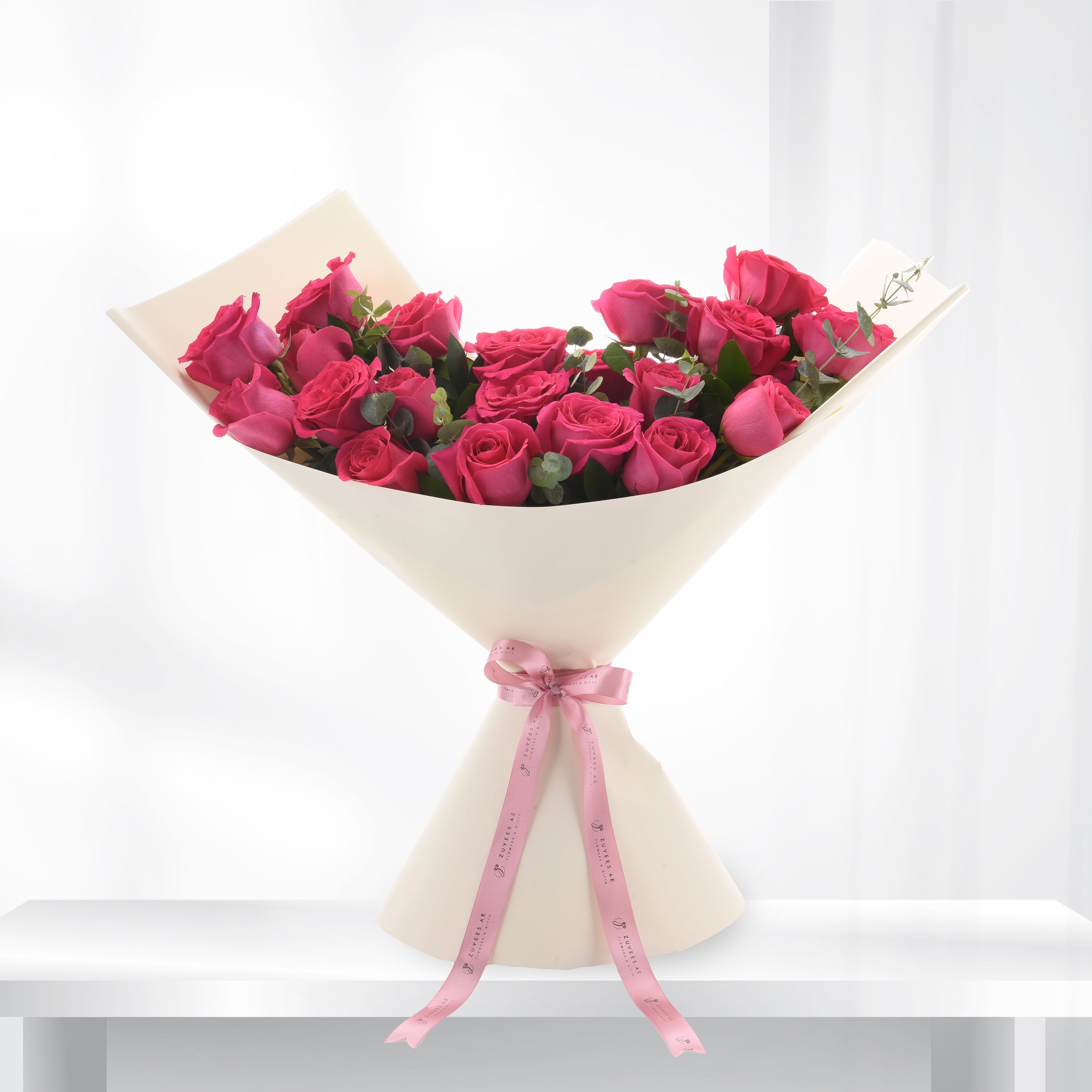Vibrant pink roses in cream wrap, accented with pink ribbon.