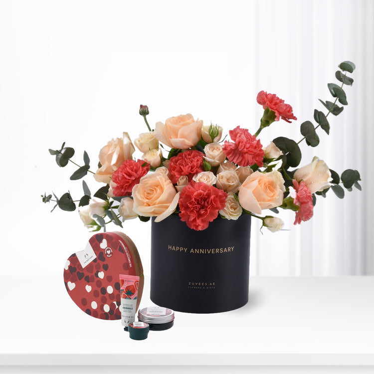 Elegant anniversary bouquet with roses and carnations in black vase, paired with strawberry-scented spa gifts.