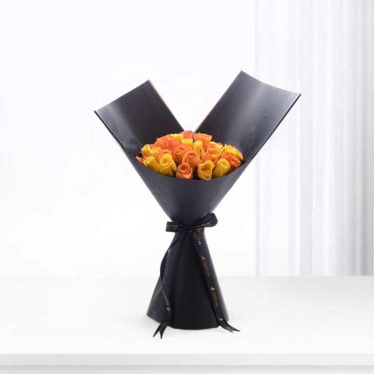 Vibrant orange-yellow roses elegantly wrapped in matte black paper with gold-trimmed ribbon.