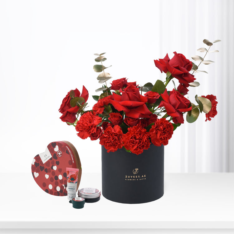 Vibrant red roses, carnations, and eucalyptus in sleek black Zuvees box with heart-shaped chocolate gift set.