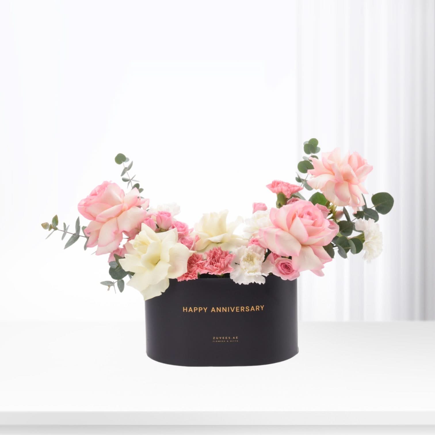 Elegant black box with "Happy Anniversary" in gold, overflowing with soft pink and white roses and eucalyptus.