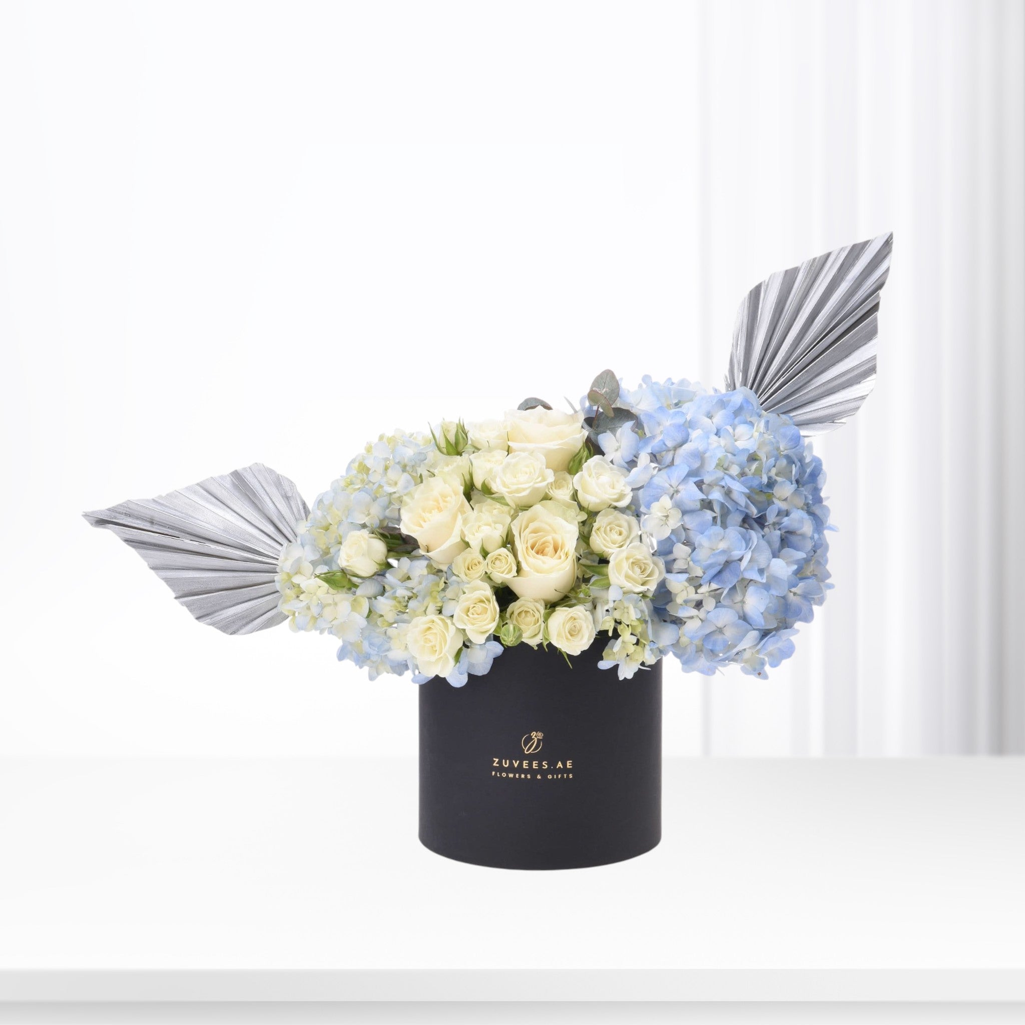 Elegant blue hydrangeas and cream roses in black box with silver fan accents.