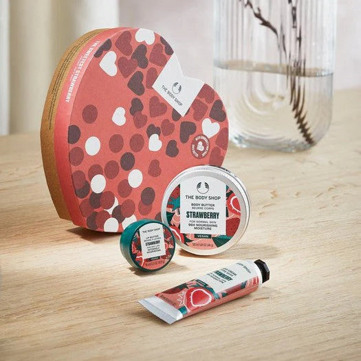 Heart-shaped gift set with strawberry-scented body butter, cream, and balm in vibrant red, white, and green packaging.
