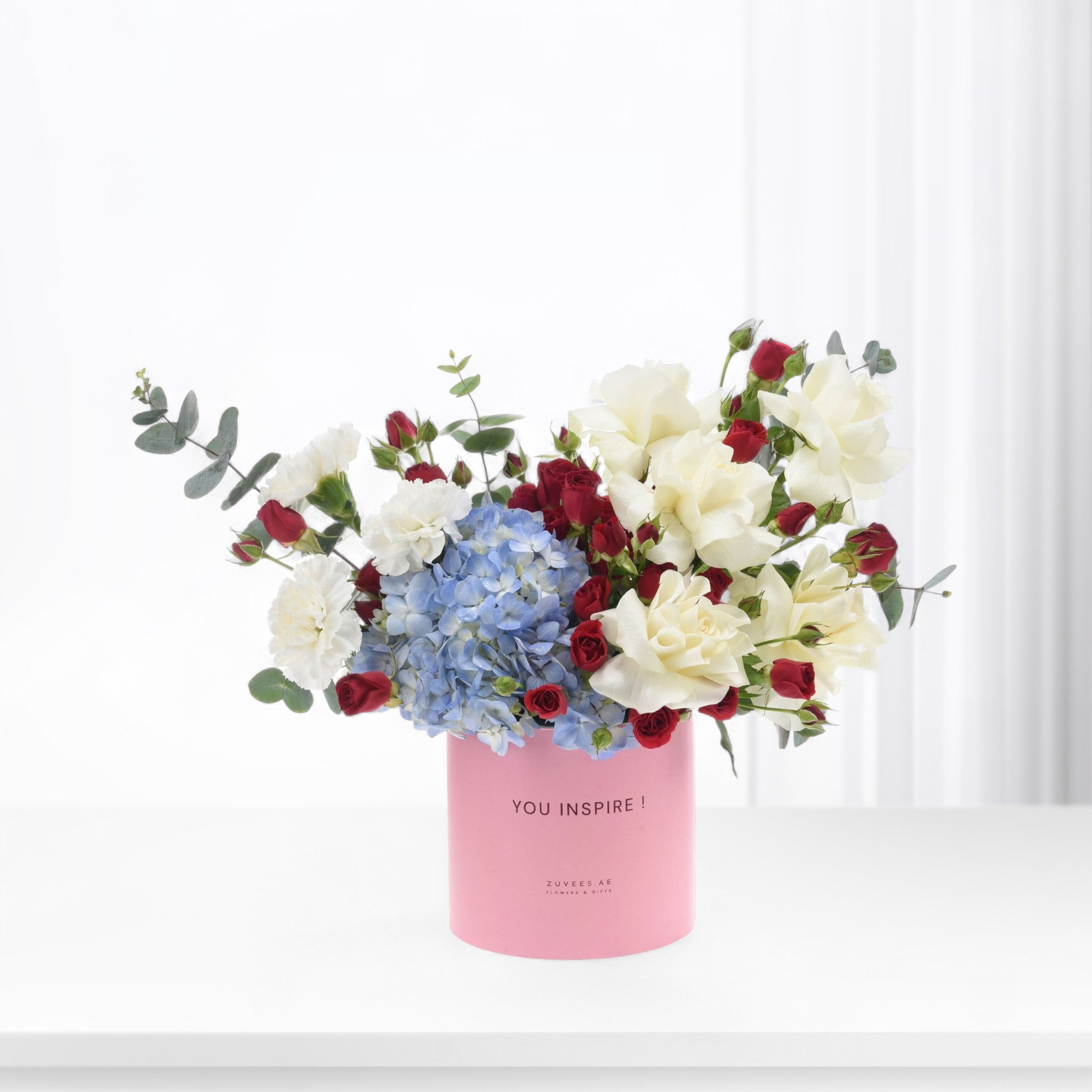 Pink vase holds red, white roses and blue hydrangeas with "YOU INSPIRE!" text.