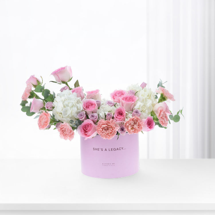 Pastel pink roses, carnations, and hydrangeas in a lavender box reading "She&