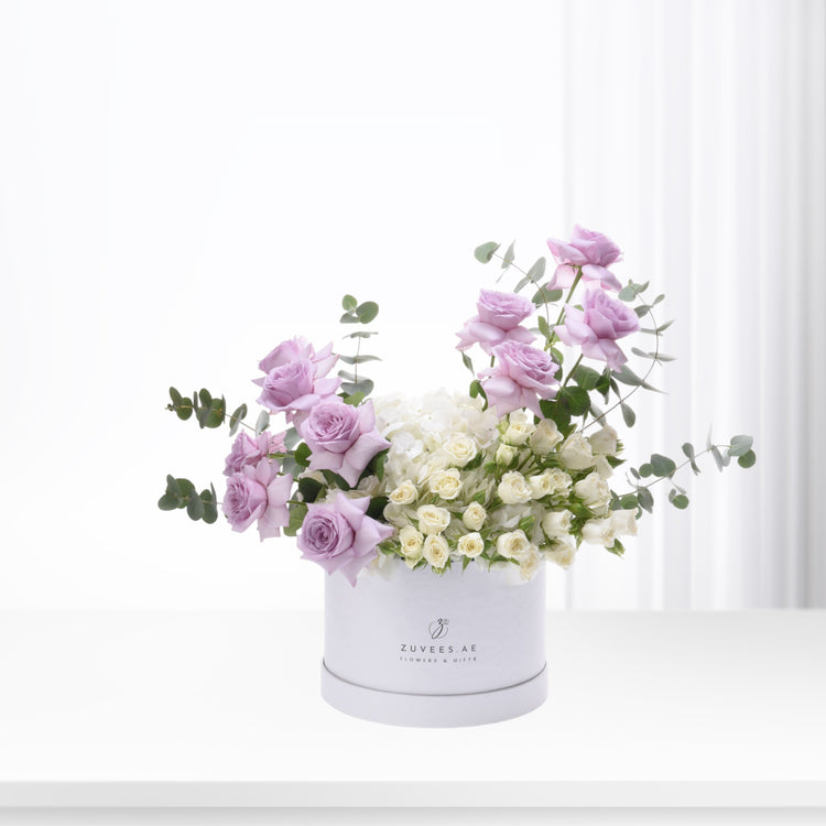 Elegant lavender roses and white blooms in a branded white box.