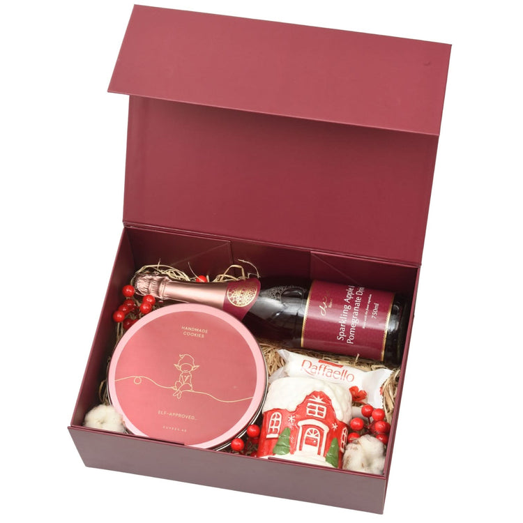 Rich burgundy gift box holds sparkling drink, cookies, Raffaello, and festive candy house.