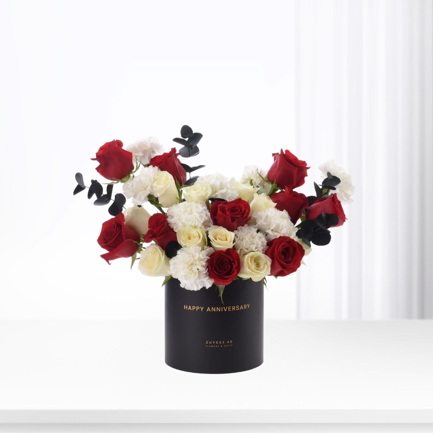 Elegant black box holds vibrant red, white roses and black eucalyptus for anniversary.