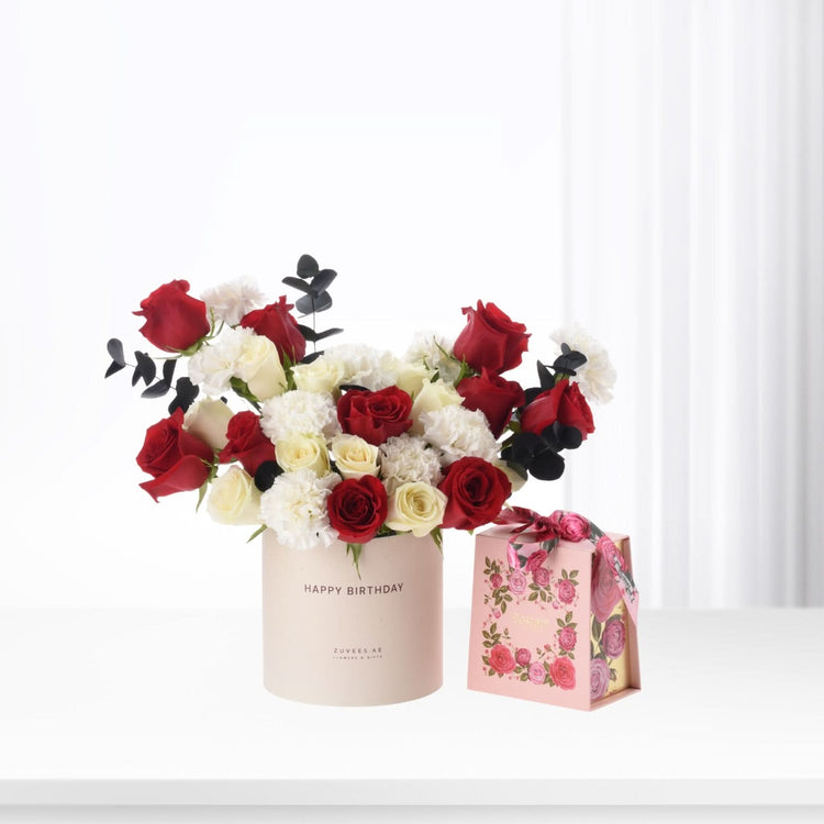 Vibrant red and white roses with black eucalyptus in blush box, beside floral gift bag.