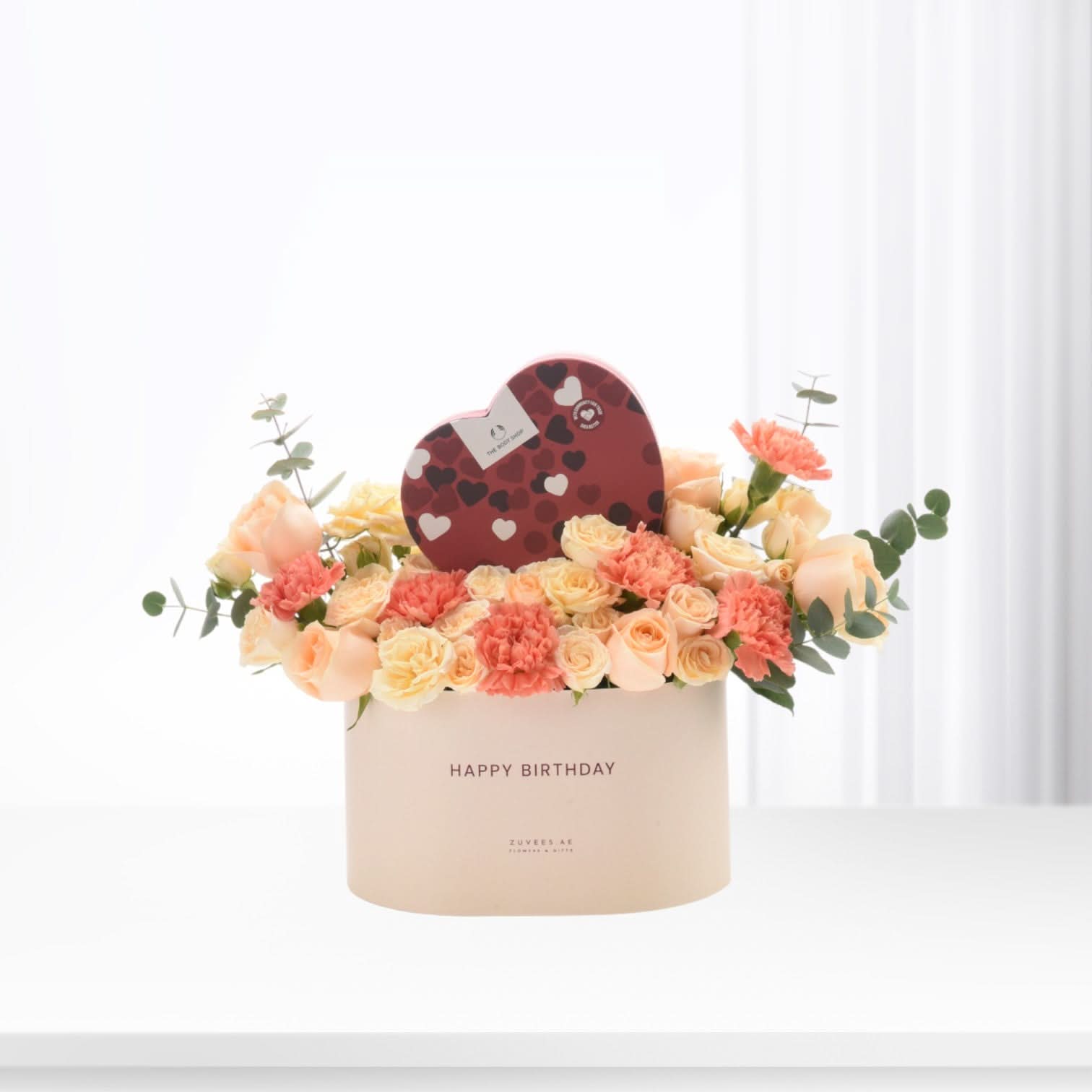 Pastel peach roses and carnations in cream box with heart chocolate gift.