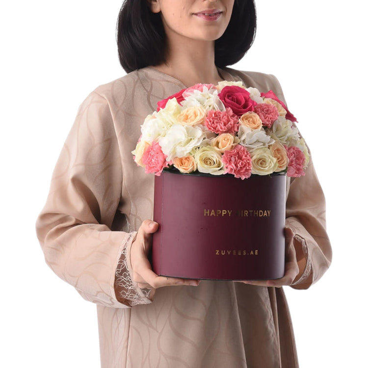 Woman holds burgundy birthday box filled with vibrant pink, peach, and white roses.