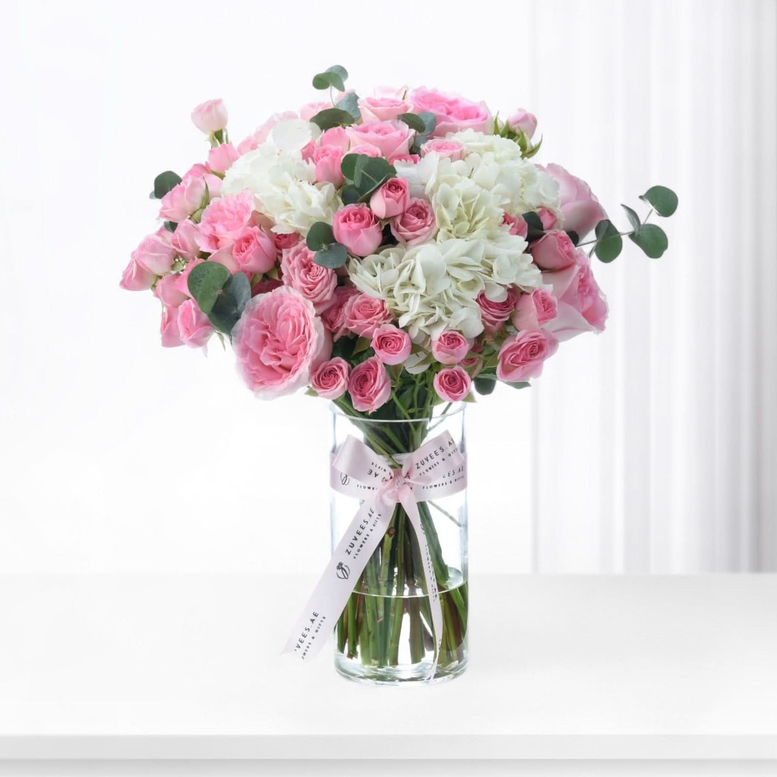 Pink roses and white hydrangeas in clear vase with branded ribbon.