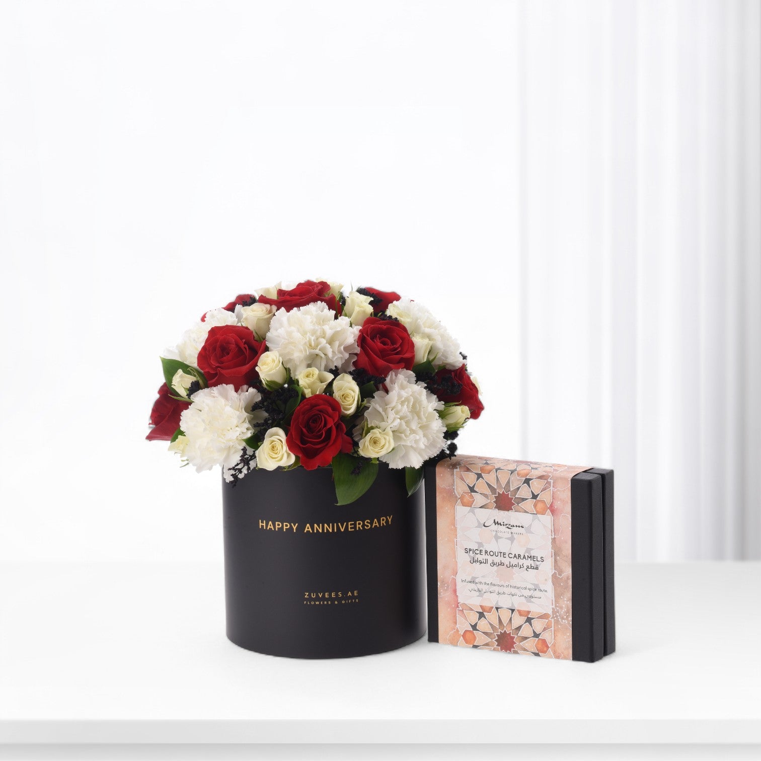 Elegant black anniversary flower box with red and white blooms beside spice caramel gift.