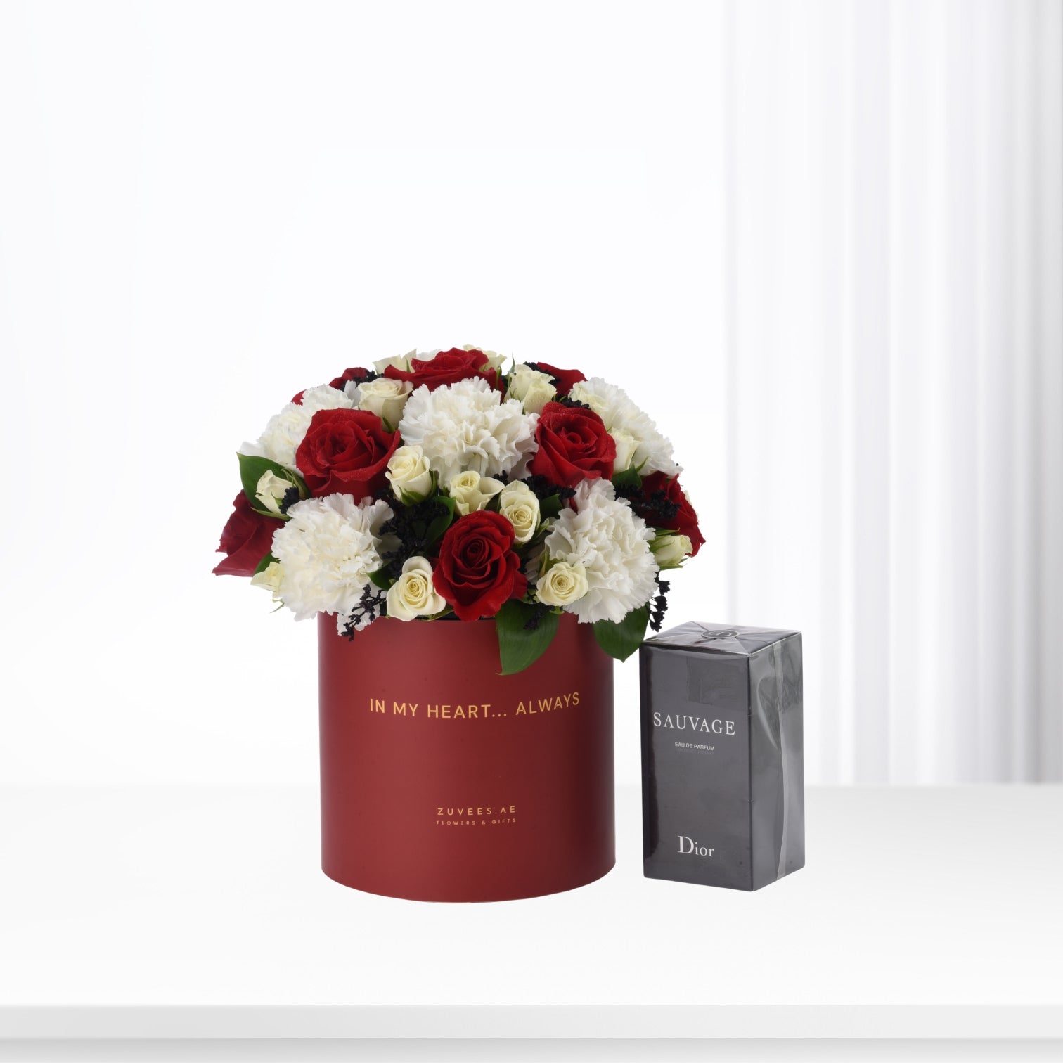 Red cylindrical box with red and white roses, beside Dior Sauvage perfume.