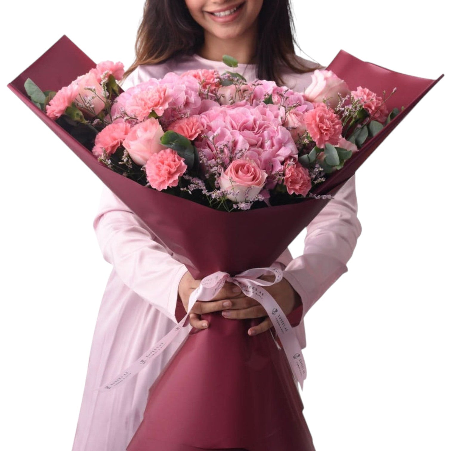 Pink roses, carnations, and hydrangeas wrapped in burgundy paper with ribbon.
