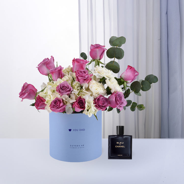 Pastel blue box holds vibrant pink roses and white hydrangeas, beside sleek Chanel perfume.