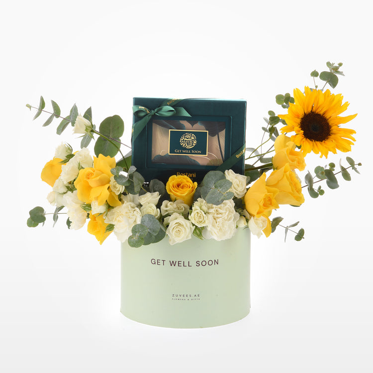Pastel green box holds vibrant yellow roses, sunflower, and eucalyptus with "Get Well Soon" gift inside.