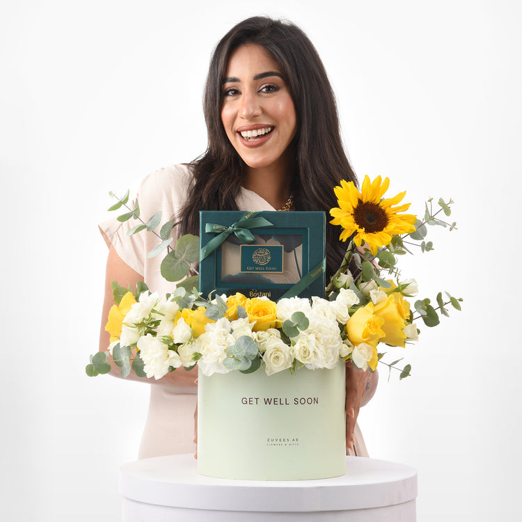 Smiling woman holds vibrant yellow and white floral gift box with "Get Well Soon" message.
