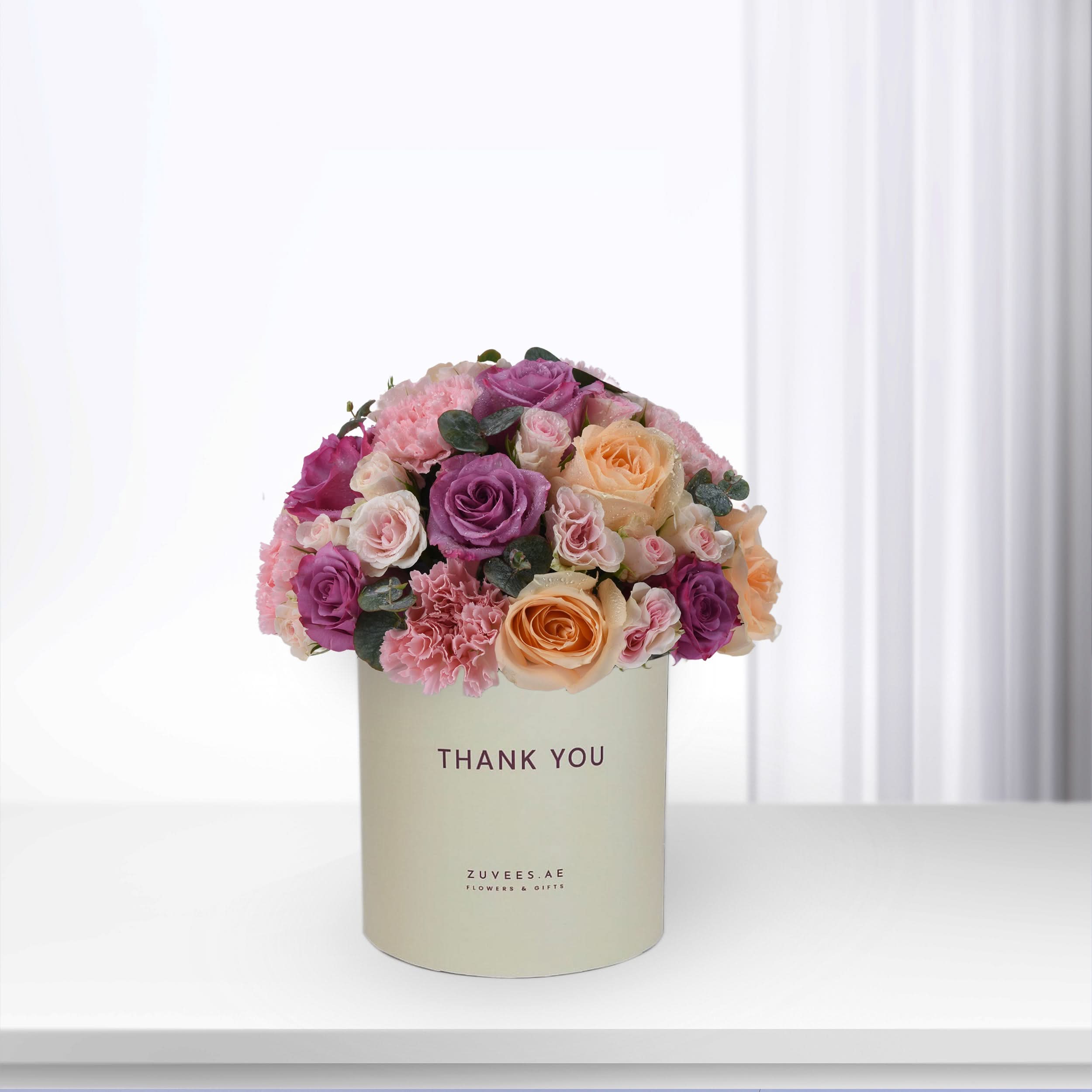 Pastel pink, purple, and peach roses in cream box reading "Thank You".