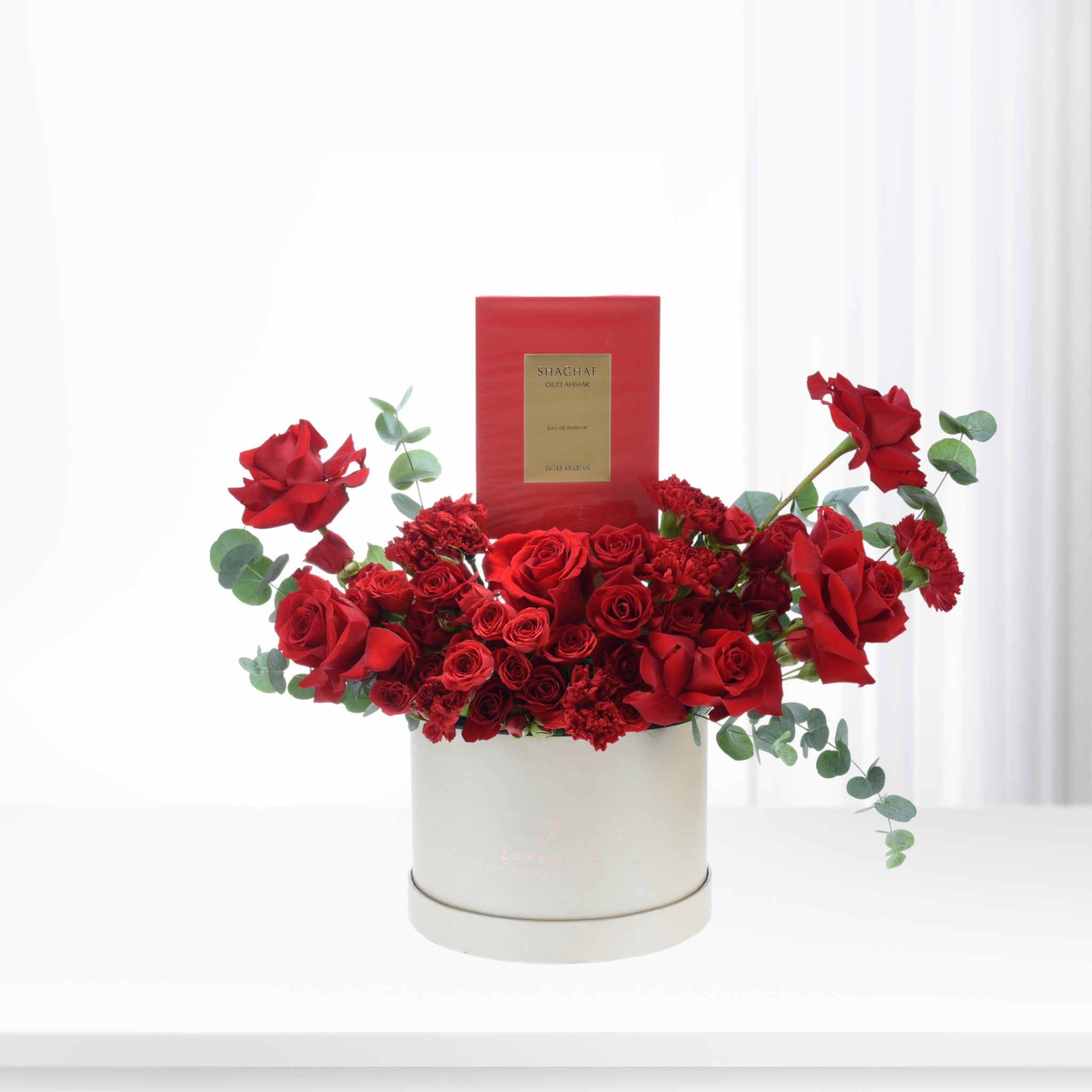 Vibrant red roses and carnations in cream box, accented with eucalyptus and luxury perfume.