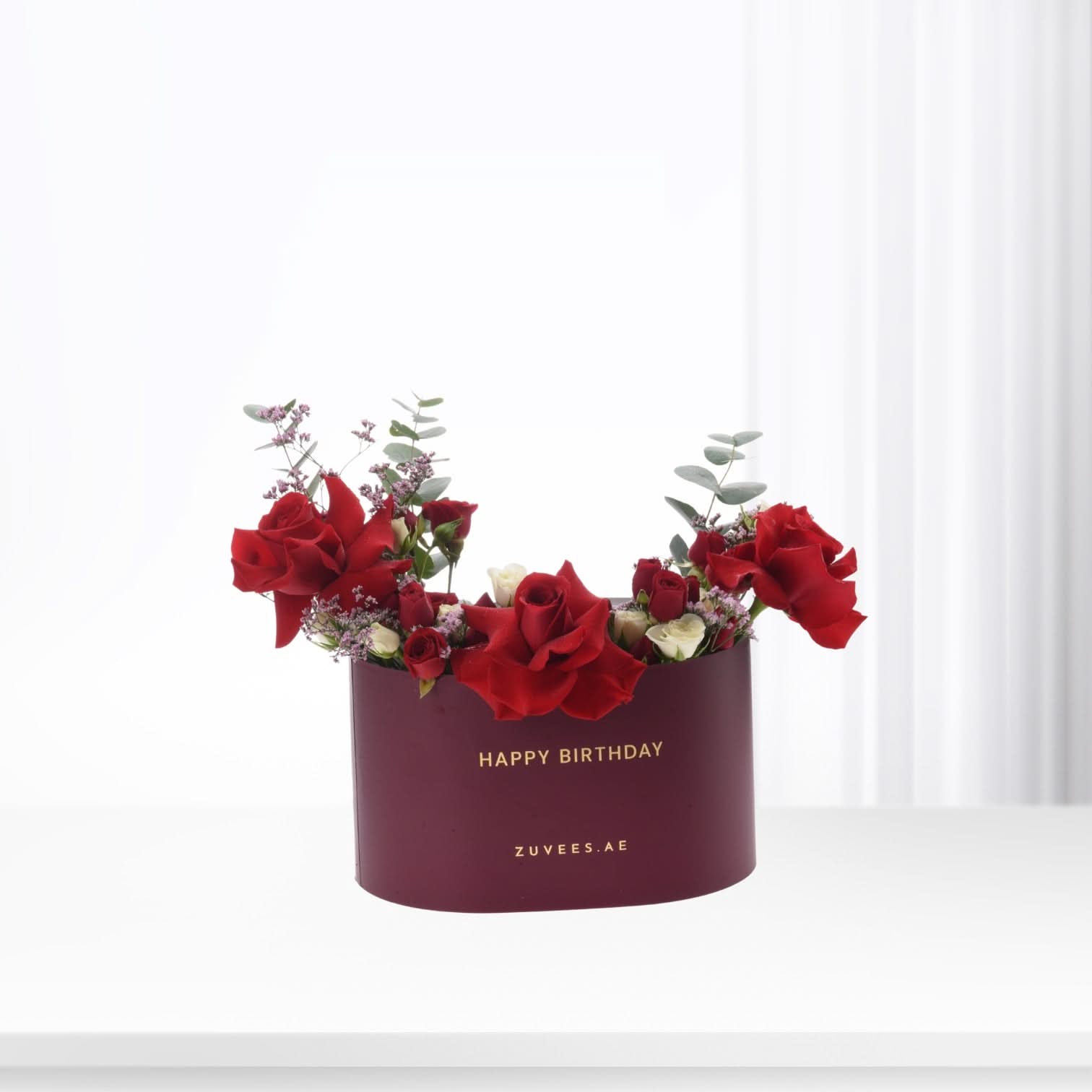 Vibrant red roses and eucalyptus in burgundy box with gold "Happy Birthday" text.