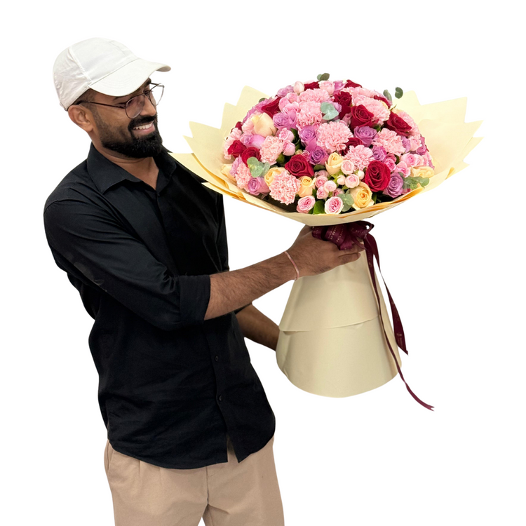 Man holds vibrant pink, red, and yellow floral bouquet wrapped in cream paper.
