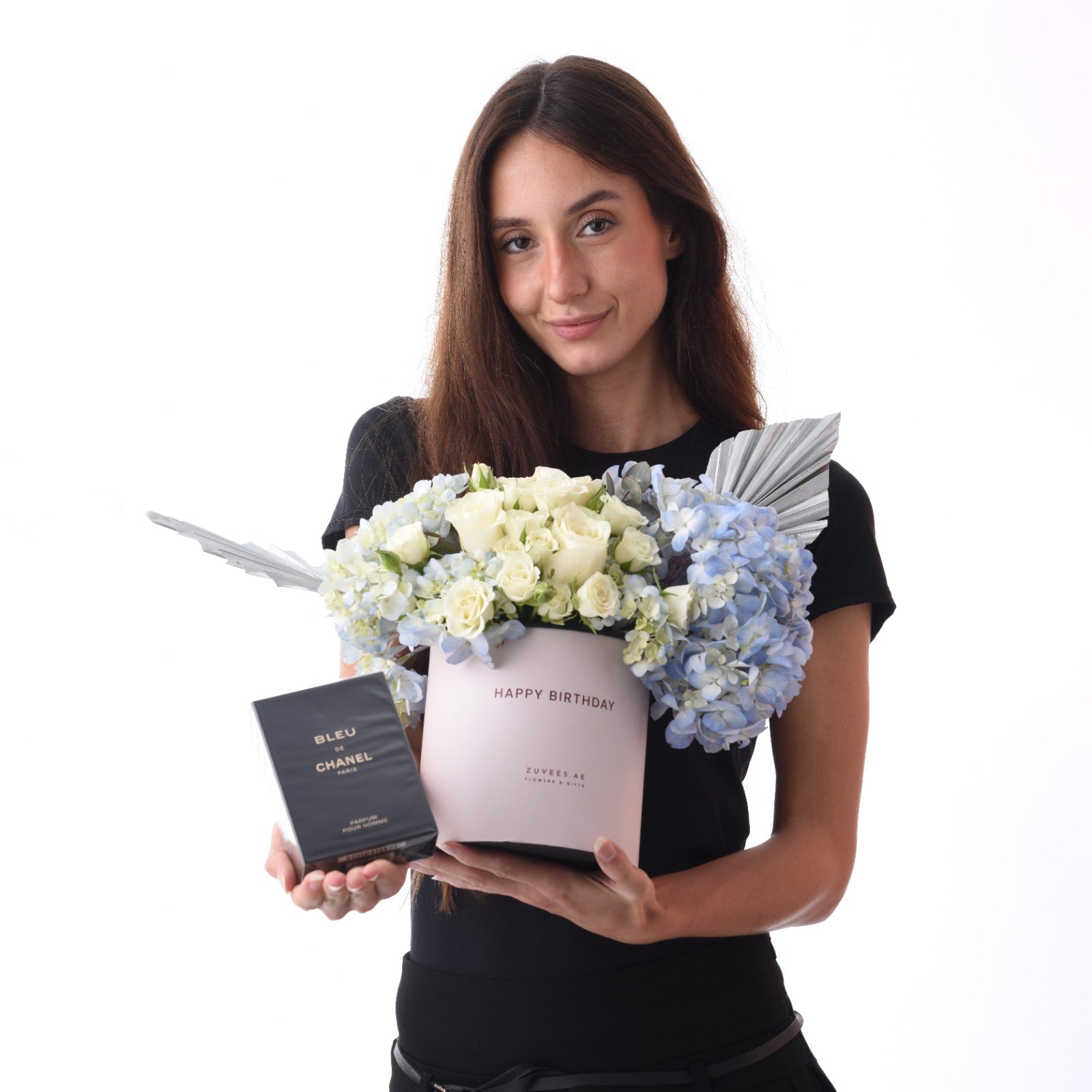 Woman holds elegant blue hydrangea and white rose bouquet in pink box with "Happy Birthday" text, alongside Bleu de Chanel perfume.