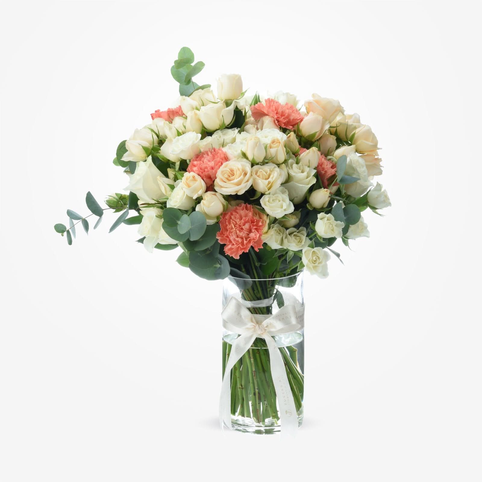 Elegant white roses and coral carnations in clear vase with ivory ribbon.