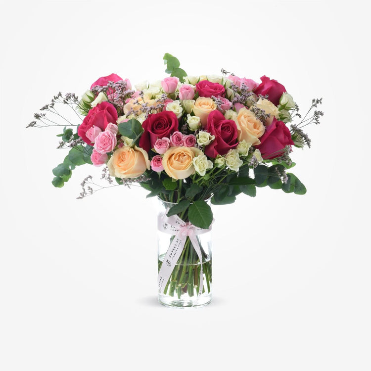 Vibrant multi-colored roses in clear vase with elegant ribbon.