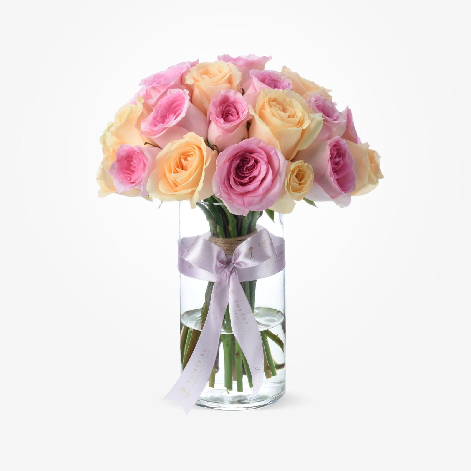 Pastel pink and peach roses in clear glass vase with lavender ribbon.