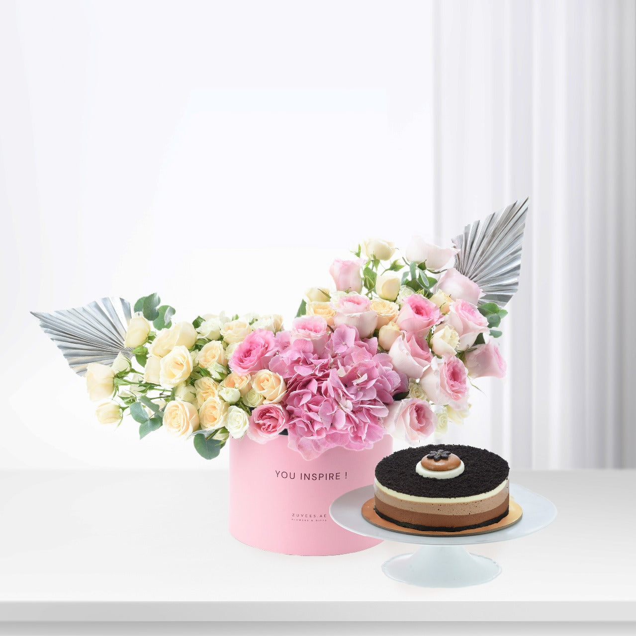 Pink floral arrangement with silver accents beside layered chocolate cake.