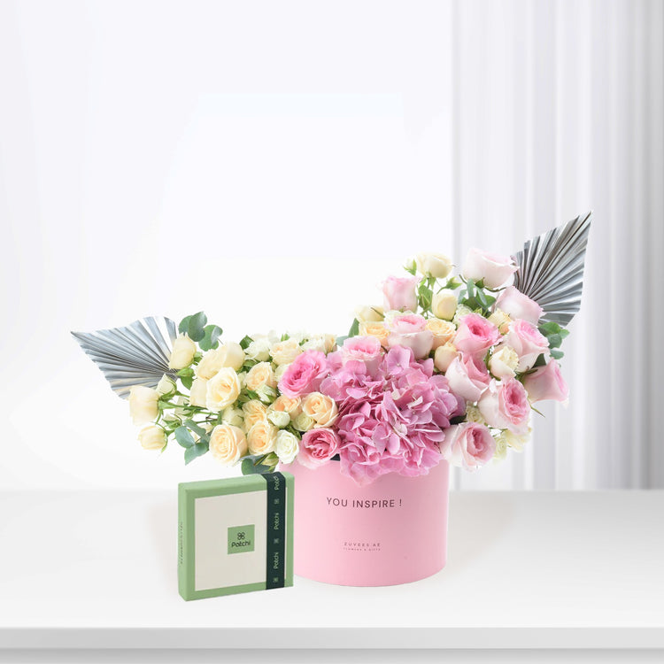 Pink box holds pastel roses and hydrangeas, accented with silver fan leaves.