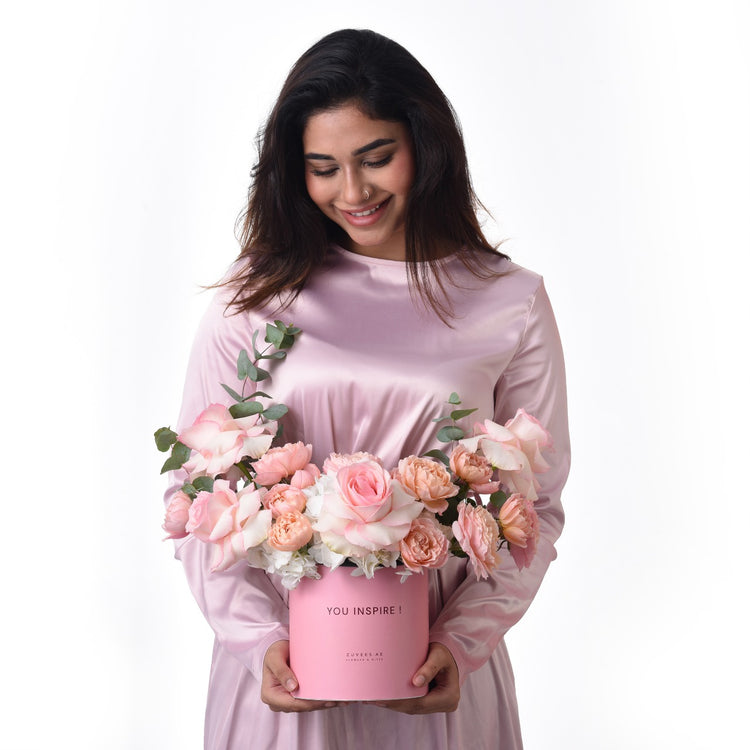 Soft pink roses in matching box, held by smiling woman in satin dress.
