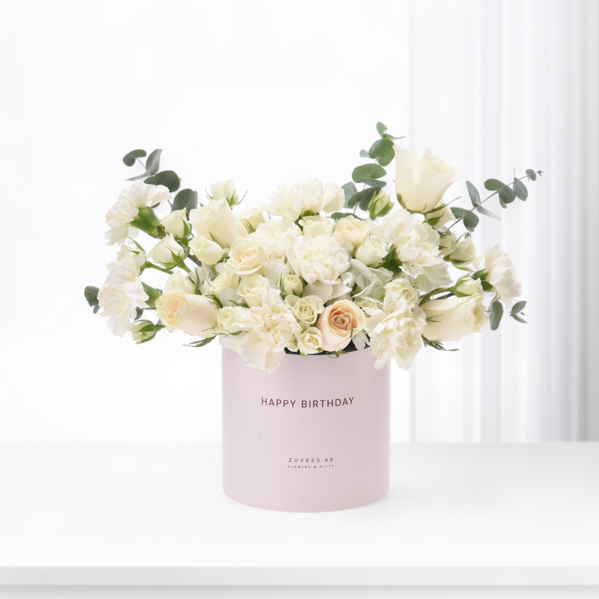 Elegant white roses and carnations in blush pink "Happy Birthday" gift box, accented with eucalyptus.