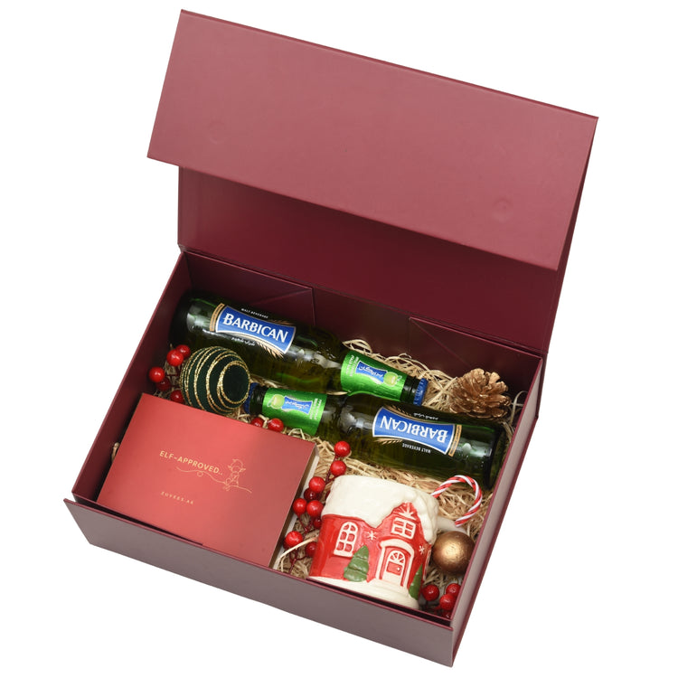 Elegant burgundy gift box with Barbican malt, festive mug, and holiday decorations.