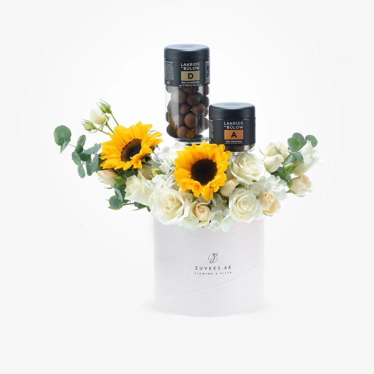White cylindrical gift box with sunflowers, roses, and two Lakrids candies.