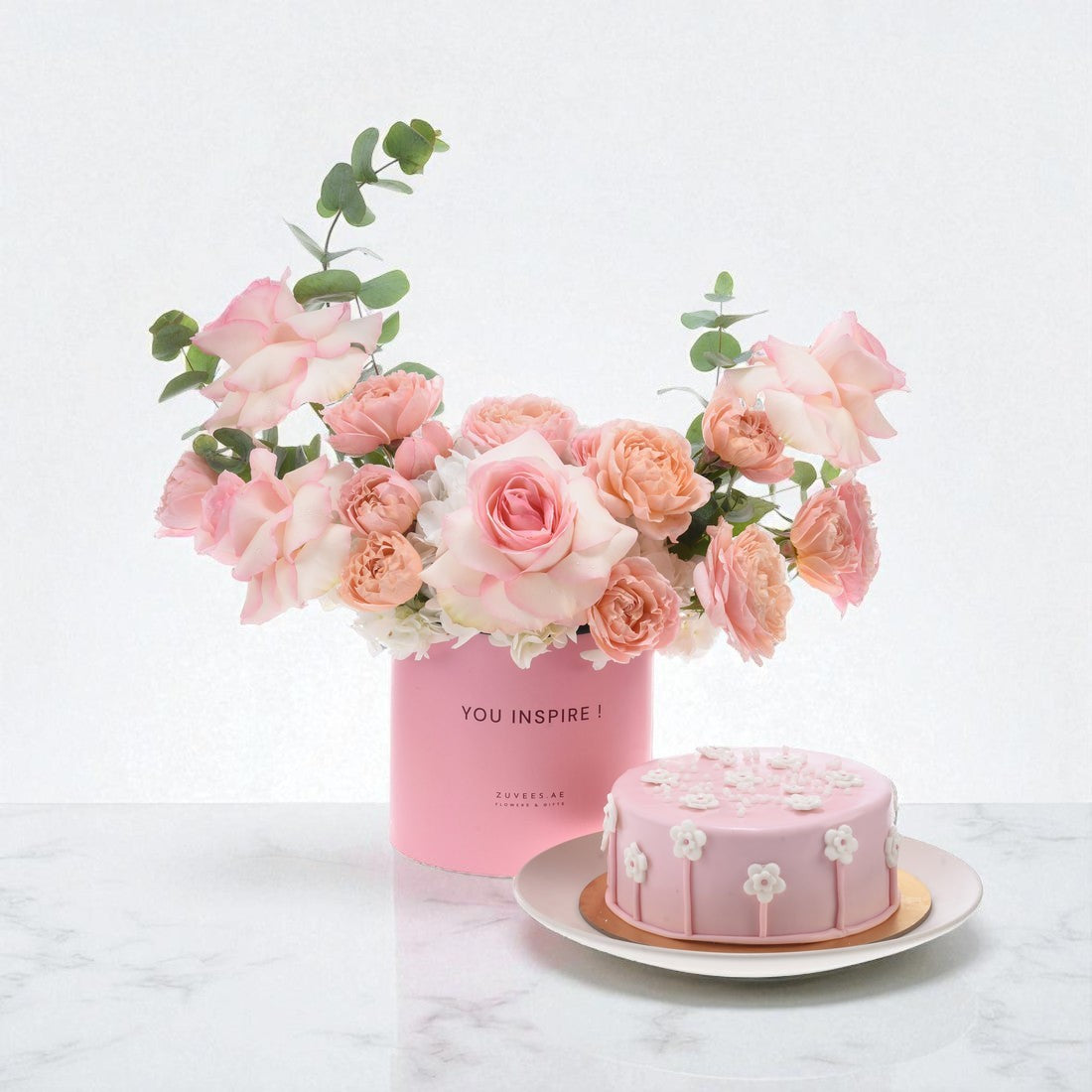 Soft pink roses and cake in matching pink box on marble.