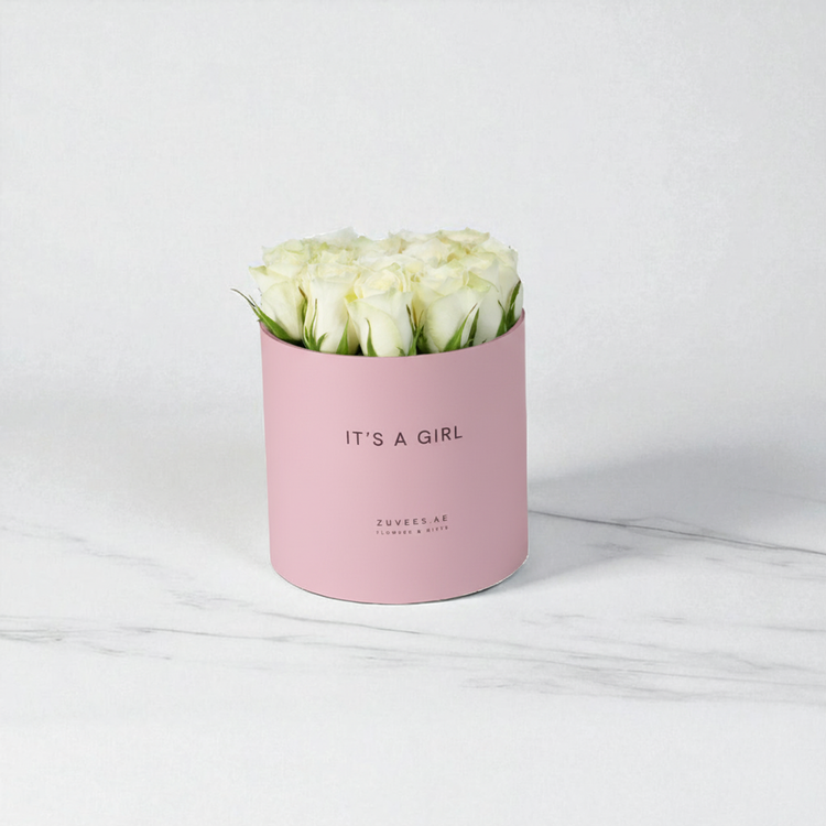 Soft pink box holds creamy white roses, “It’s a Girl” text, elegant marble backdrop.