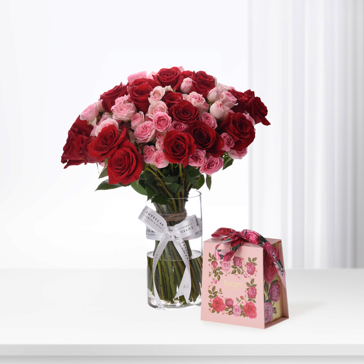 Vibrant red and pink roses in clear vase, beside floral gift box.