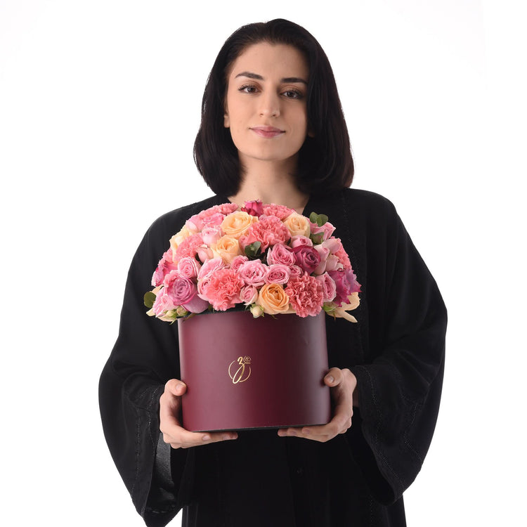 Woman holds burgundy box of vibrant pink, peach, and magenta roses.