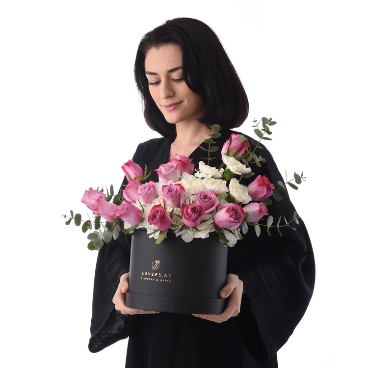 Woman holds elegant black box with pink roses, white blooms, and eucalyptus, branded Zuvees.ae.