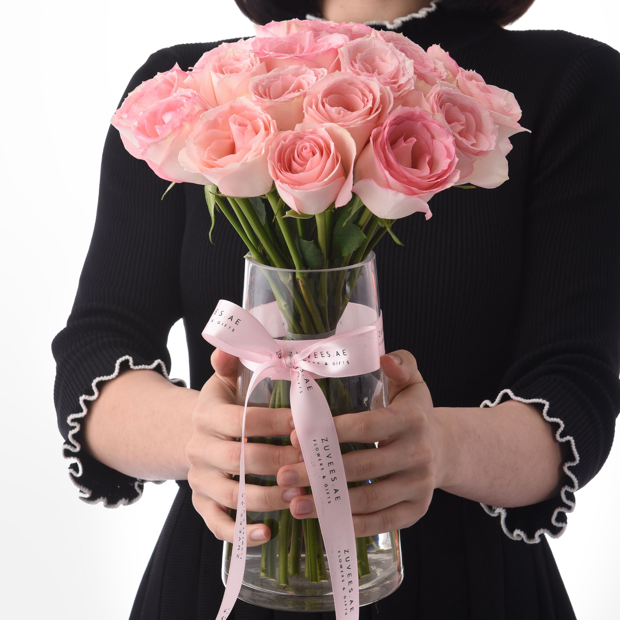 Pink roses in clear vase, ribbon-tied, held by person in black ribbed top.