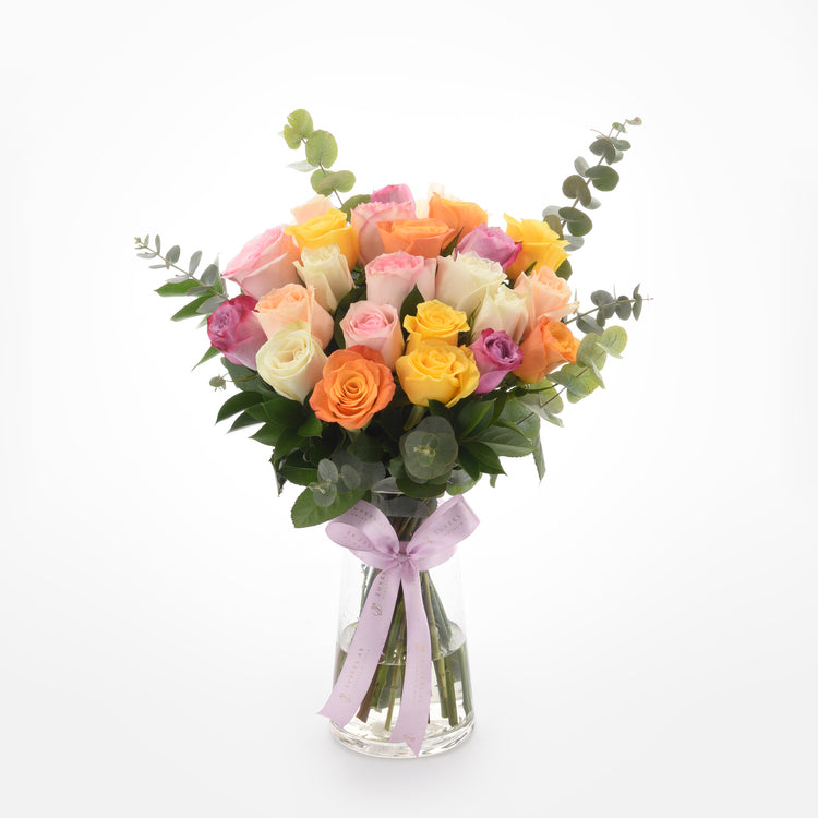 Vibrant multicolor roses in clear vase, accented with eucalyptus and lavender ribbon.