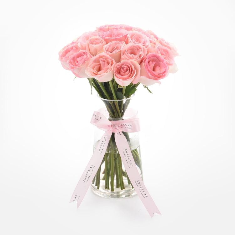 Soft pink roses in clear vase, elegantly tied with branded ribbon.