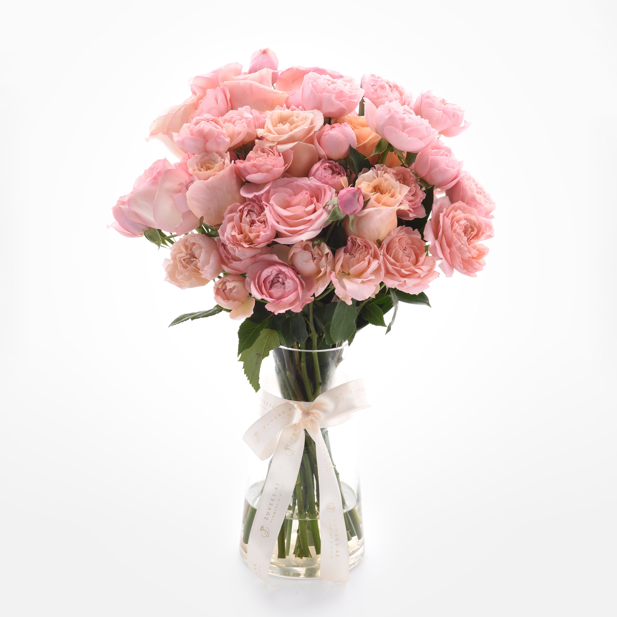 Soft pink roses in clear vase, elegantly tied with branded cream ribbon.
