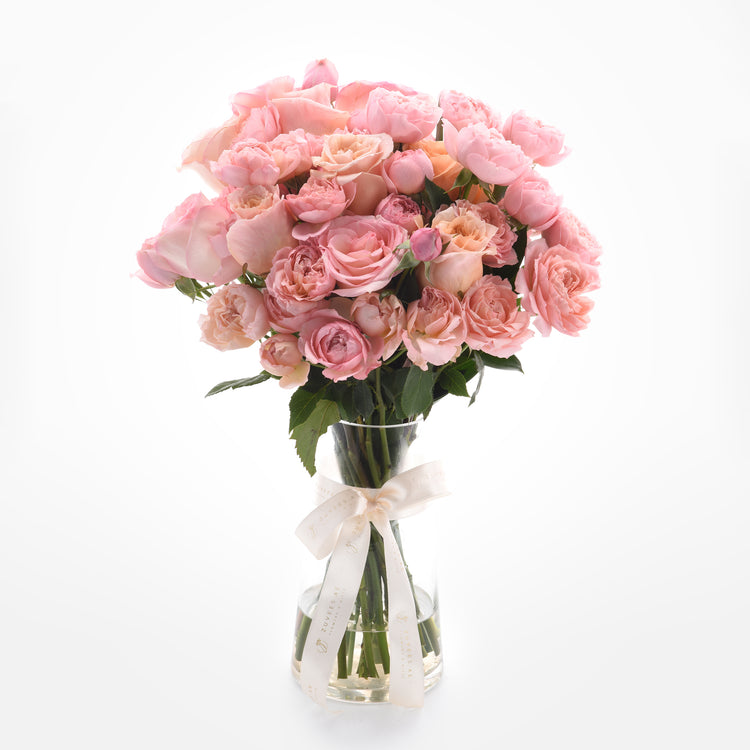 Soft pink roses in clear vase, elegantly tied with branded cream ribbon.