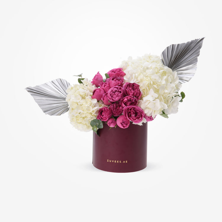 Vibrant pink roses and white hydrangeas in burgundy box with silver fan accents.
