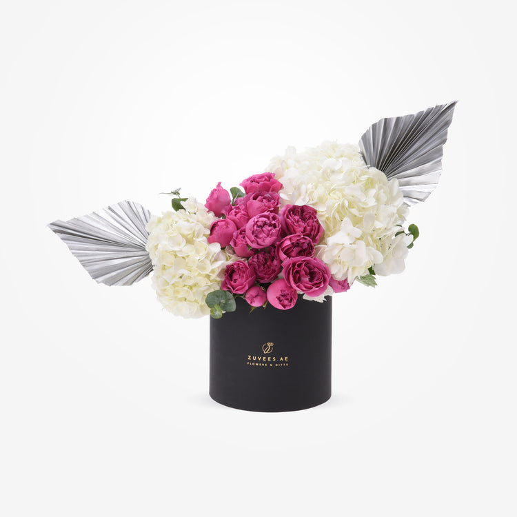 Elegant black box holds vibrant pink roses and white hydrangeas, accented with metallic silver fan leaves.