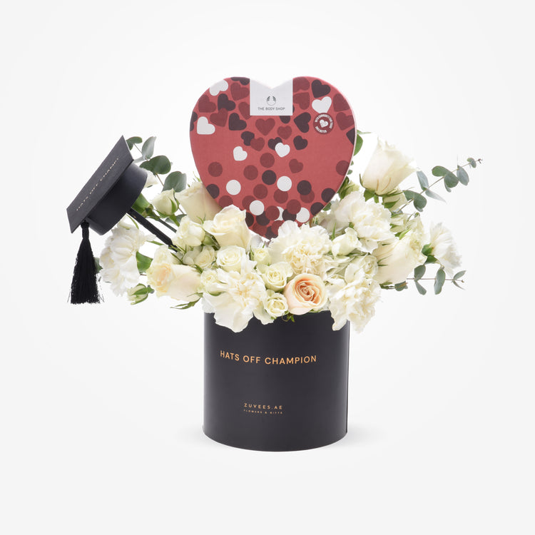 Elegant white roses and eucalyptus in black "Hats Off Champion" vase with heart-shaped chocolate box.